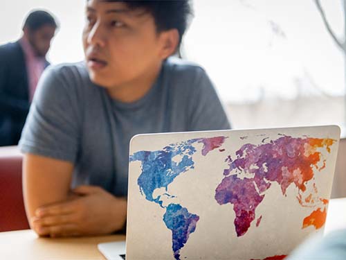 a student sits at a laptop decorated with a multicolored graphic map of the world decal