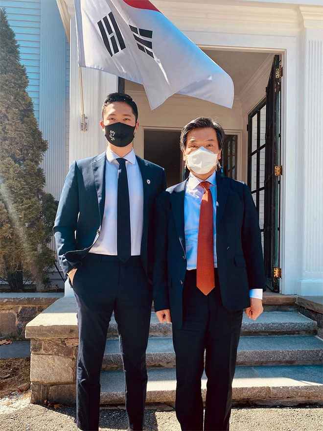 Sam Hyun, MBA/MPP'22, with the South Korean Consul General outdoors, under a South Korean flag