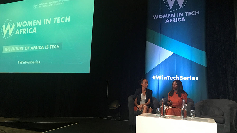 Amrote Abdella, MA SID'07, sitting behind a white desk with another female speaker in front of a Women in Tech Africa banner 