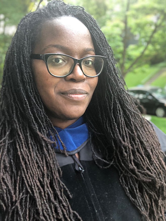Andréa Harris, PhD'21, in a black graduation robe and glasses