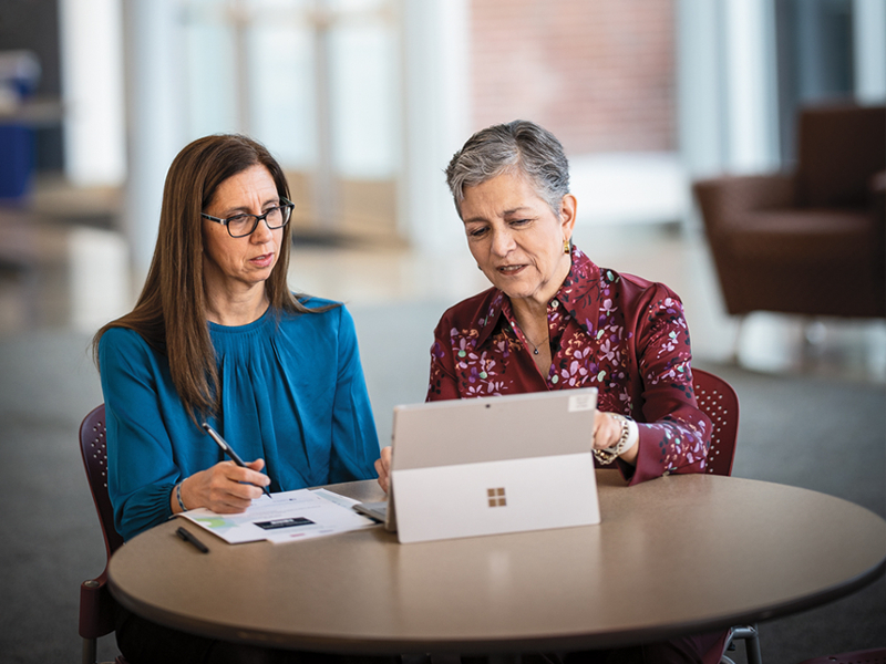 Pam Joshi and Dolores Acevedo-Garcia discuss research while sitting at a table with a laptop